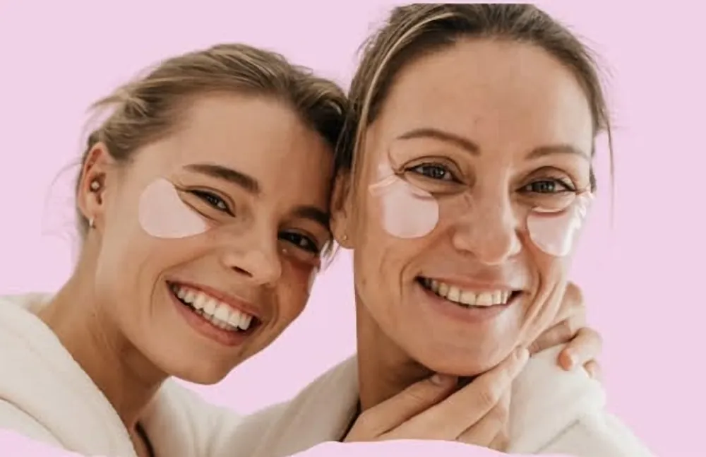 Two smiling women wearing under-eye patches during their skincare routine